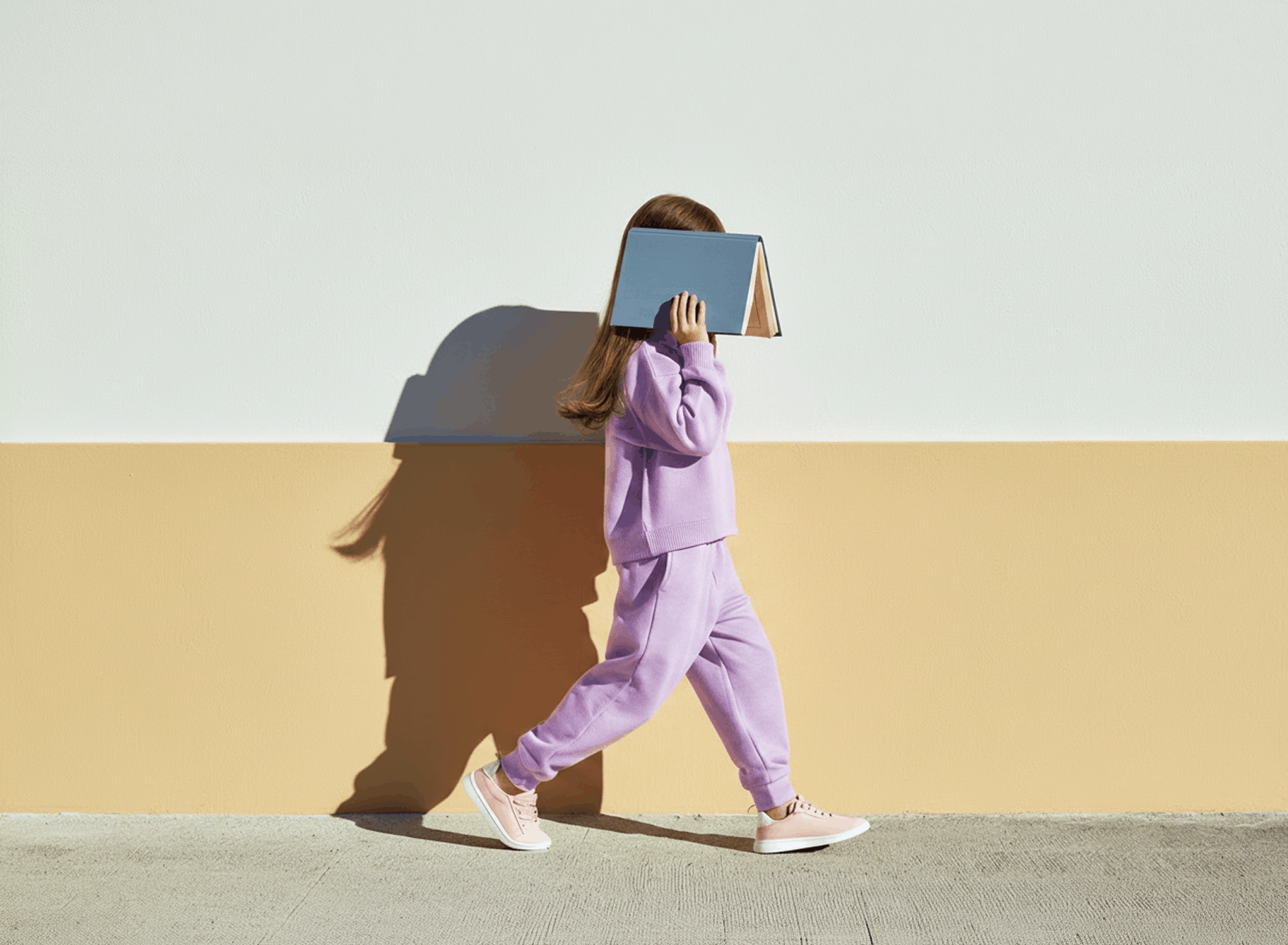 Child in pastel Back-to-School outfit walking past coloured walls with a notebook over their face